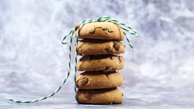 American chocolate chip cookies stacked on top of each other with green thread on a gray background. Traditional rounded crunchy dough with chocolate chips. Bakery. Delicious dessert, pastries