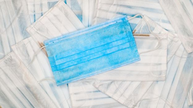 Coronavirus protection. Many antiviral protective medical face masks with ear loops spread out on a blue background. Surgical mask background. Respiratory syndrome, coronavirus disease COVID-19
