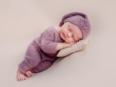 Newborn in knitted suit resting on tiny pillow under head