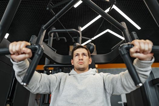 Young fit bodybuilder man doing arms workout training in the gym on machine, close up