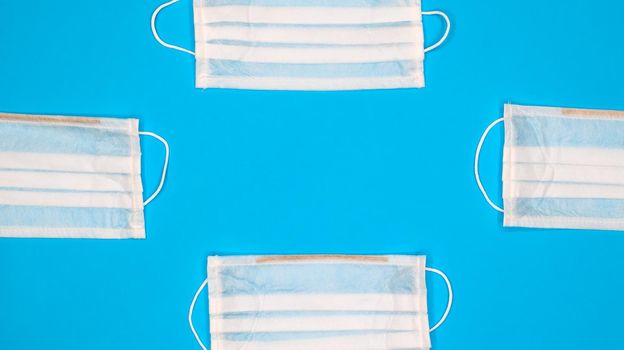 Many antiviral protective medical face masks with earloops are set against a blue background. Surgical mask background. Respiratory syndrome, coronavirus disease COVID-19. Copy space.