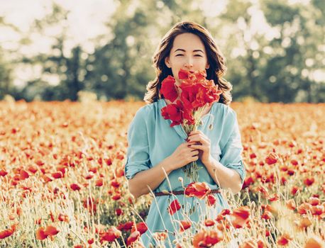 Beautiful young woman standing with bouquet of red poppies in flowers meadow in spring.