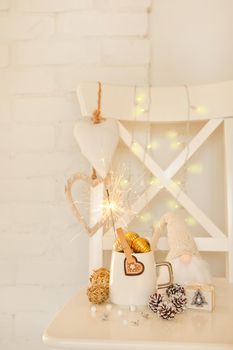 White cup with golden balls and sparklers. Cute gnome with long beard. white cristmas hearts, pine cones and warm lights on brick wall