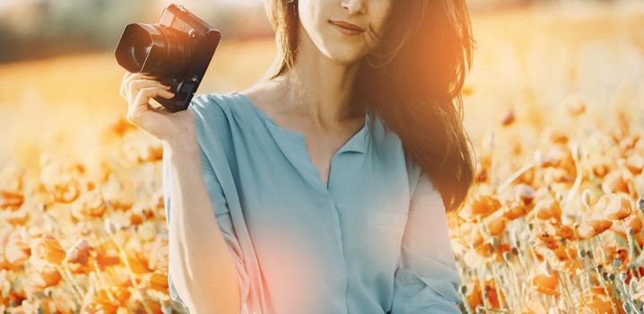 Smiling photographer woman with photo camera standing in poppy flowers meadow.