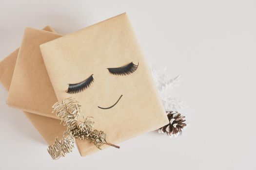 gift boxes with kraft paper on gray background, original gift decor with false eyelashes and minimalistic eco-friendly christmas decor, spruce branch and pine cone