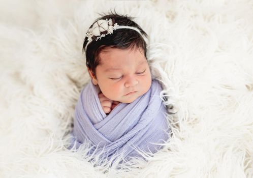 Smiling newborn in knitted hat on white fluffy blanket