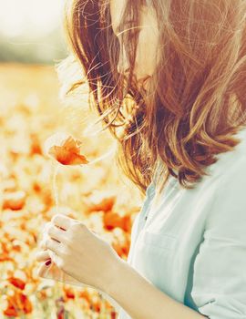 Beautiful young woman holding poppy flower in spring meadow.