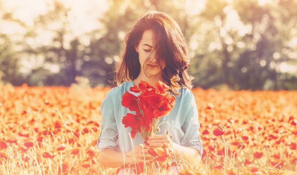 Beautiful romantic young woman standing in red poppies field with bouquet of flowers in summer outdoor.