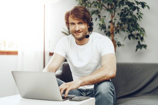 Young man businessman with headset working on laptop from home. Home office concept