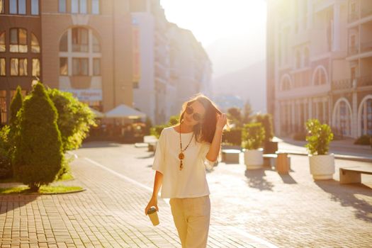 Stylish attractive brunette young woman walking with paper cup of coffee in city street.