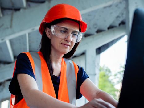 Girl foreman with laptop at construction site. A female engineer works on a computer on the background of a building under construction.