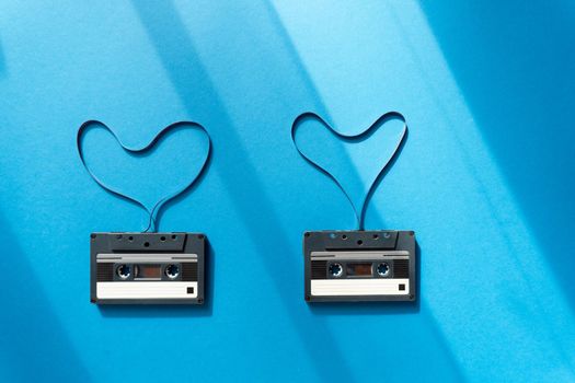 Two old record cassettes with magnetic tape in the shape of heart on classic blue background on sunlights and shadows. Minimal creative concept, love.
