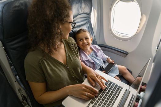 Happy mother and daughter looking at each other while on an airplane. Trip and family concept