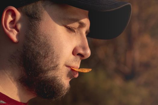 Bearder Man in forest eating chips. In park image outdoors with blurred background.