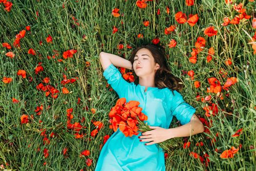 Beautiful brunette young woman lying and relaxing on summer poppy flowers meadow.