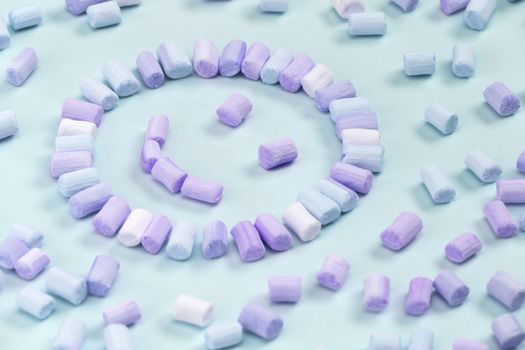 Top view of the multi-colored marshmallows which lies in the shape of a smiley or sun on a one-color pink background.