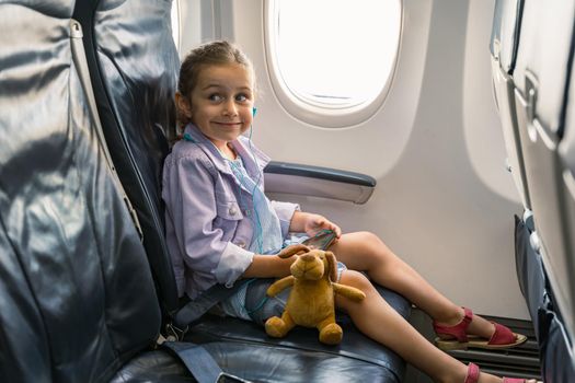 Smiling cute girl using headphones and a smartphone while flying on an airplane. Trip concept