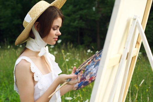 woman with a palette of paints painting a picture outdoors close-up. High quality photo