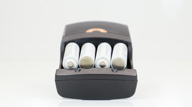 Fast charging of AA batteries. Rechargeable batteries in a black charger with four battery cells on a white background