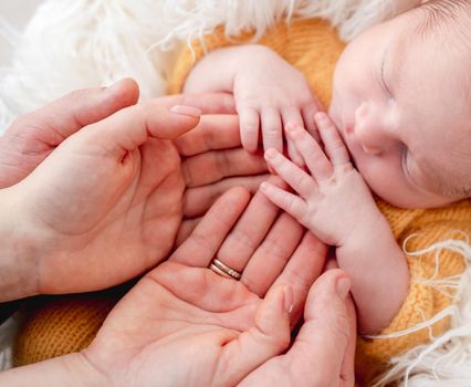 Sleeping newborn baby holding open palms of parents