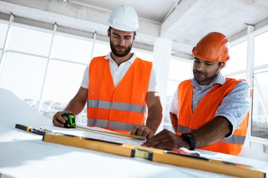 Two young engineers man looking at project plan on the table in construction site
