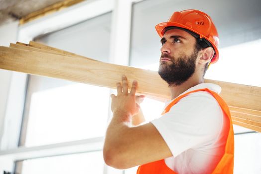 Builder man in hardhat carrying timber on building site, close up portrait