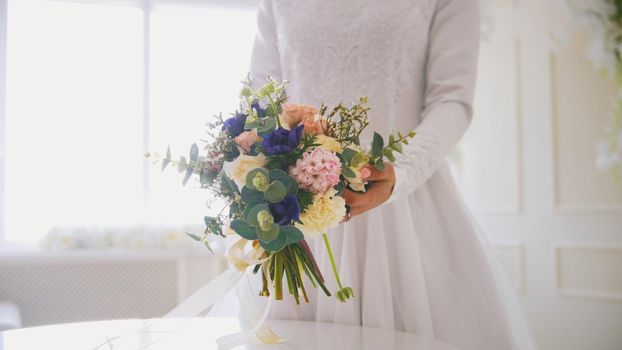 Hands of muslim bride in white dress holding the bouquet of flowers, horizontal