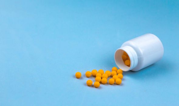 Yellow pills and plastic white bottle. Blue background with copy space for text