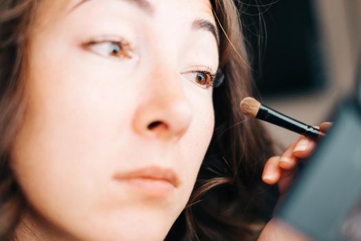 Beautiful young woman applying eyeshadow cosmetics with brush, natural makeup for eyes.