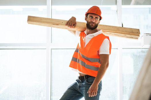 Builder man in hardhat carrying timber on building site, close up portrait