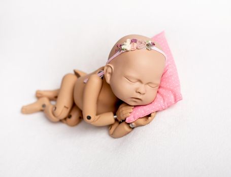 Accurate doll of newborn baby on pink pillow for photo practicing, on white background