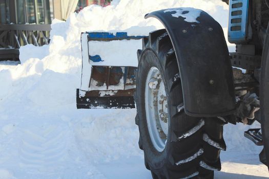Clearing snow from the road with bulldozer in the city in winter, focus on blade and wheel, urban landscape