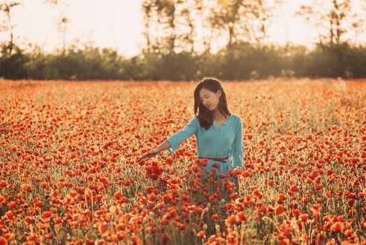 Romantic beautiful girl enjoying flower poppy meadow in summer.