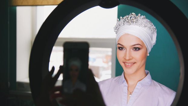 Female hands shooting on smartphone happy muslim bride with professional make up and tiara, close up