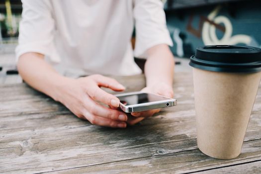 Unrecognizable young woman texting a message while sitting with cup of coffee in cafe.