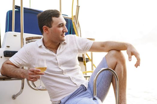 Young man holding a glass of wine on an open deck of a cruise boat, close up