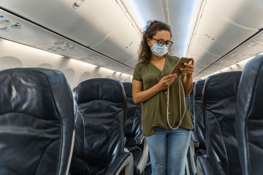 Pretty lady in glasses standing in the aisle on an airplane and holding a smartphone. Trip concept