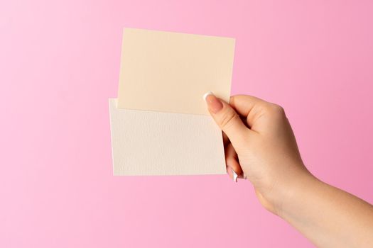 Woman hand showing blank business card on pink background. Close up.