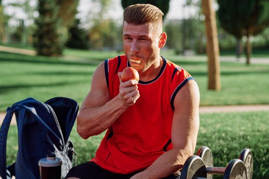 sporty man resting in the park on a bench having a snack. High quality photo