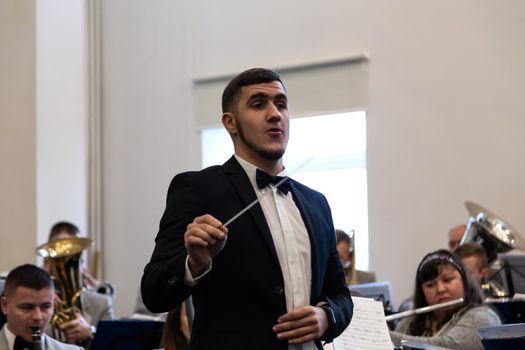 KOROSTEN - NOV, 10, 2019: Young guy orchestra conductor in a black suit. In the background is an orchestra