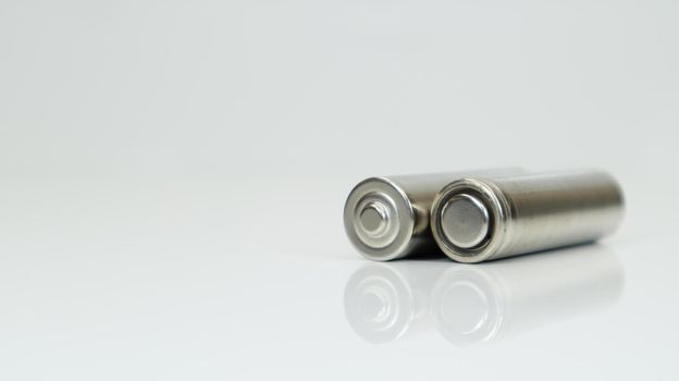 AA alkaline rechargeable batteries on white glossy background with reflection. Close up two empty batteries with copy space