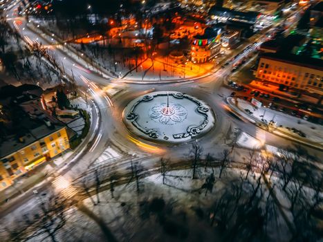 Aerial view of roundabout road with circular cars in small european city at winter night, long exposure. Kyiv region, Ukraine