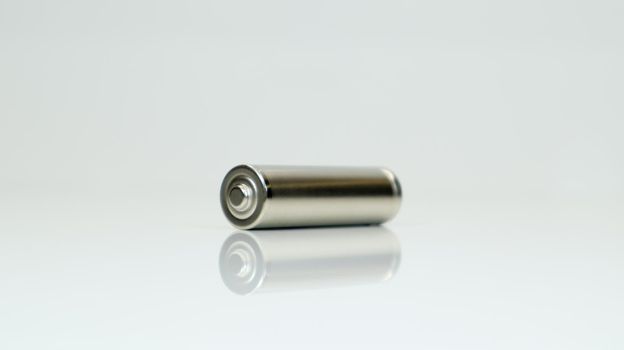 AA alkaline rechargeable battery on white glossy background with reflection. Close one empty battery with copy space