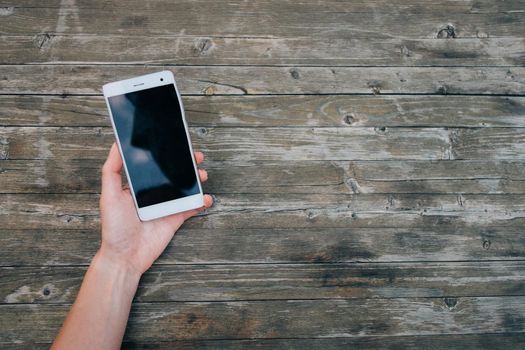 Point of view of female hand with smartphone on wooden background, mockup.