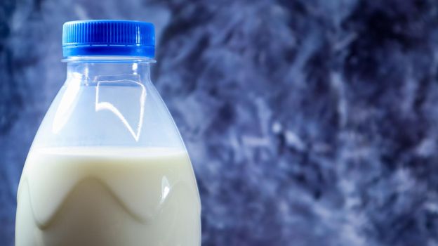 A plastic bottle of fresh regular milk on a dark gray marbled or concrete background. Close-up front view. World milk day concept. Nutrient fluid. Copy space
