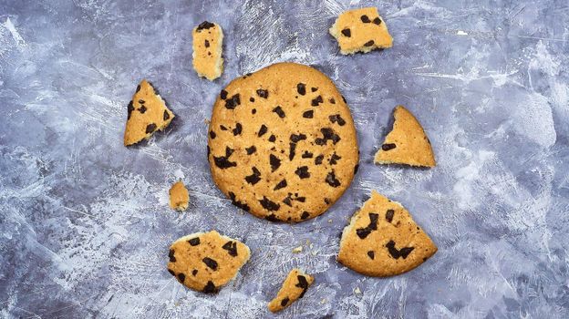 One soft freshly baked chocolate chip cookie with crumbs and chunks on a gray marble kitchen countertop. American traditional pastry, dessert. Delicious sweet food. Flat lay