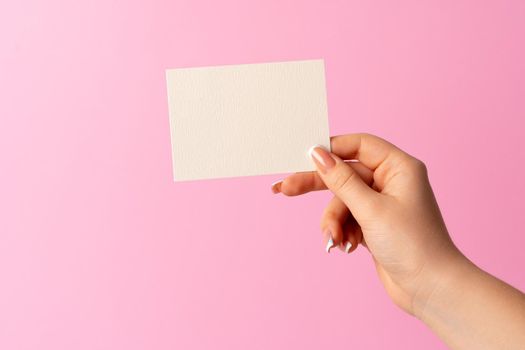 Woman hand showing blank business card on pink background. Close up.