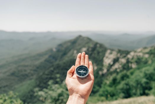 Travel magnetic compass on palm female hand on background of mountain ridge in summer outdoor, point of view.