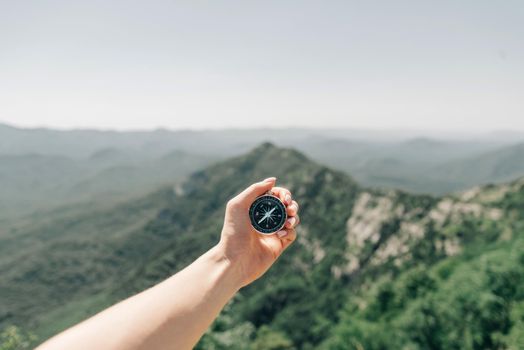 Female hand with magnetic compass high on background of summer mountain ridge, point of view.