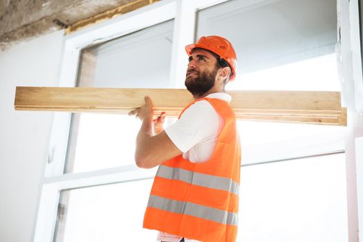 Builder man in hardhat carrying timber on building site, close up portrait